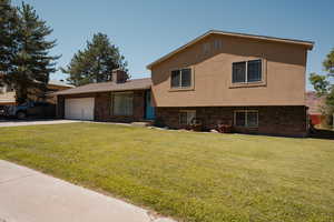 Tri-level home featuring a front yard, brick and stucco siding, a chimney, and driveway