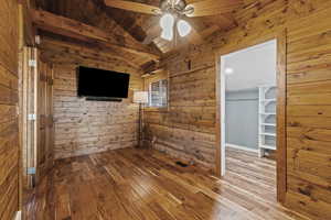 Unfurnished bedroom featuring hardwood / wood-style floors, ceiling fan, wood ceiling, a spacious closet, and wood walls