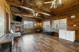 Office area featuring dark wood-type flooring, wooden walls, a fireplace, wood ceiling, and a ceiling fan