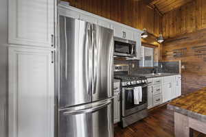 Kitchen with stainless steel appliances, white cabinets, dark wood-style floors, and tasteful backsplash