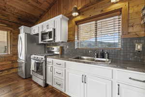 Kitchen with wood walls, dark countertops, stainless steel appliances, lofted ceiling, and white cabinets