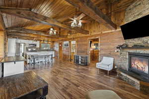 Living room featuring dark wood-style flooring, a wooden ceiling with exposed beams, a stone fireplace, wood walls, and a ceiling fan