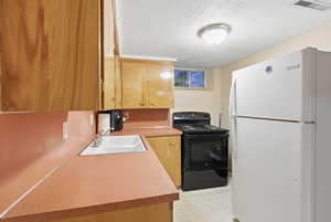 Kitchen featuring freestanding refrigerator, electric range, a textured ceiling, and light countertops