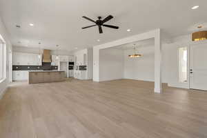 Unfurnished living room with recessed lighting, light wood-style floors, a ceiling fan, and a chandelier