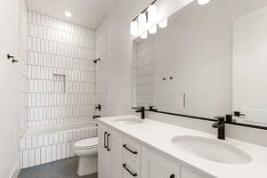 Bathroom with double vanity, tiled shower / bath combo, dark tile patterned flooring, and recessed lighting