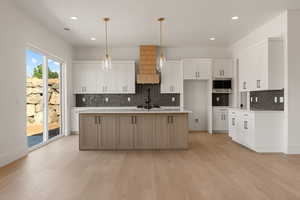 Kitchen featuring an island with sink, hanging light fixtures, white cabinets, recessed lighting, and light wood-type flooring