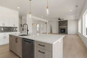 Kitchen featuring white cabinets, stainless steel dishwasher, light wood finished floors, decorative light fixtures, and backsplash