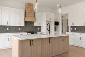 Kitchen featuring white cabinetry, an island with sink, decorative backsplash, light stone countertops, and light wood-style floors
