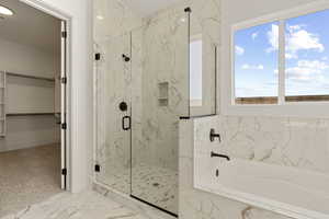 Bathroom featuring a bath, a spacious closet, light marble finish floors, and a marble finish shower
