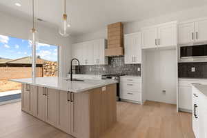 Kitchen with white cabinetry, light stone counters, decorative light fixtures, stainless steel appliances, and light wood-type flooring