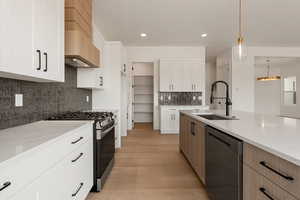 Kitchen with appliances with stainless steel finishes, white cabinets, light stone countertops, hanging light fixtures, and light wood-type flooring