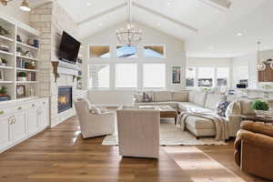 Living area featuring a chandelier, beamed ceiling, light wood-type flooring, a stone fireplace, and recessed lighting