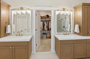 Bathroom with light tile patterned floors, two vanities, a shower stall, and a walk in closet