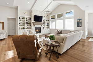 Living area featuring high vaulted ceiling, hardwood / wood-style flooring, a stone fireplace, beam ceiling, and a chandelier