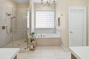 Full bathroom with vanity, a shower stall, a garden tub, light tile patterned floors, and a chandelier