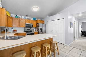 Kitchen featuring light countertops, light tile patterned flooring, appliances with stainless steel finishes, a kitchen bar, and a textured ceiling