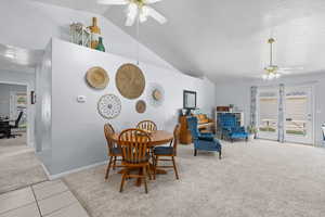Dining space featuring light carpet, ceiling fan, lofted ceiling, light tile patterned floors, and a textured ceiling