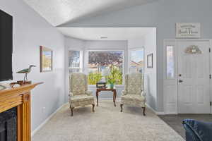Living area featuring a textured ceiling, vaulted ceiling, a high end fireplace, and carpet