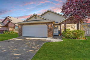 Single story home featuring an attached garage, a lawn, concrete driveway, roof with shingles, and brick siding