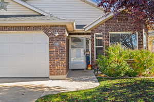 Property entrance with brick siding, a garage, and roof with shingles