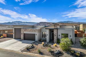 View of front facade featuring stone siding, stucco siding, a garage, and a mountain view