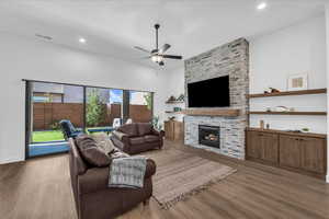 Living room with a stone fireplace, wood finished floors, a ceiling fan, and recessed lighting