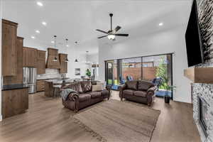 Living room with light wood-style floors, ceiling fan, a stone fireplace, recessed lighting, and a chandelier