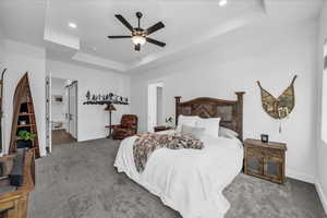 Carpeted bedroom with a tray ceiling, a ceiling fan, and recessed lighting