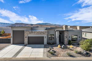 View of front of property with stucco siding, a garage, a mountain view, concrete driveway, and stone siding