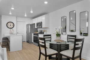 Kitchen featuring a breakfast bar area, light wood-style flooring, white cabinets, appliances with stainless steel finishes, and recessed lighting