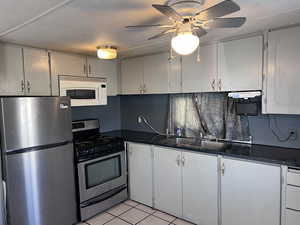 Kitchen with stainless steel appliances, light tile patterned floors, dark countertops, gray cabinets, and a textured ceiling