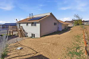Rear view of property with stairway, solar panels, brick siding, and a deck