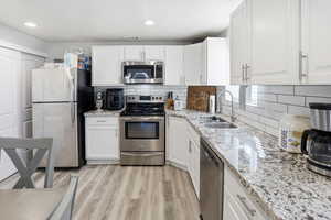 Kitchen featuring white cabinetry, stainless steel appliances, light stone counters, and recessed lighting