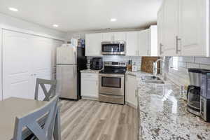 Kitchen with appliances with stainless steel finishes, light stone counters, tasteful backsplash, white cabinets, and light wood-style flooring