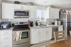 Kitchen with appliances with stainless steel finishes, white cabinetry, tasteful backsplash, light stone counters, and light wood finished floors