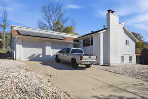 View of side of property featuring brick siding, driveway, a chimney, solar panels, and a garage