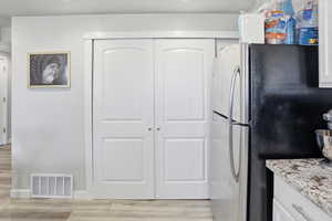 Kitchen featuring white cabinetry, freestanding refrigerator, light wood-type flooring, light stone countertops, and a textured wall