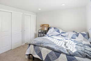 Bedroom with light colored carpet, two closets, and recessed lighting