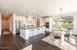 Kitchen featuring white cabinets, a kitchen bar, appliances with stainless steel finishes, a center island with sink, and hanging light fixtures