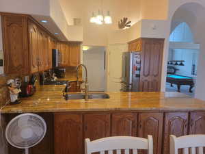 Kitchen with billiards, brown cabinets, light stone countertops, stainless steel appliances, and pendant lighting