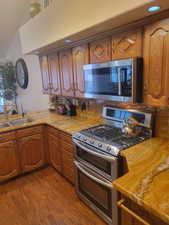 Kitchen with stainless steel appliances, light stone counters, brown cabinetry, and dark wood-style flooring