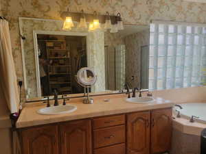 Bathroom with a walk in closet, double vanity, a bath, a stall shower, and wallpapered walls