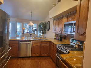 Kitchen with appliances with stainless steel finishes, light stone counters, dark wood-style flooring, and brown cabinets