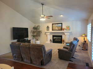 Carpeted living room featuring lofted ceiling, ceiling fan, and a fireplace