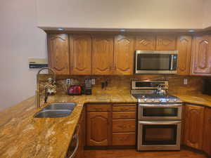 Kitchen featuring stainless steel appliances, brown cabinets, and light stone countertops