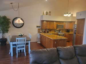 Kitchen featuring open floor plan, high vaulted ceiling, a chandelier, brown cabinets, and dark wood-type flooring