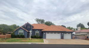 Mediterranean / spanish home with a tile roof, an attached garage, driveway, and stucco siding