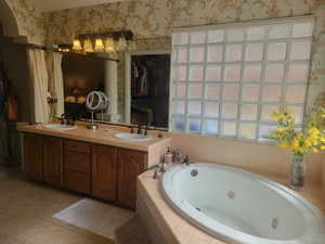 Full bathroom featuring a jetted tub, double vanity, light tile patterned flooring, wallpapered walls, and a spacious closet