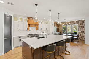 Kitchen with brick wall, light wood-style floors, glass insert cabinets, white cabinets, and a kitchen bar