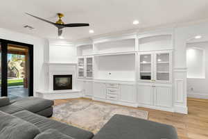 Living area featuring light wood-type flooring, a glass covered fireplace, crown molding, a ceiling fan, and recessed lighting